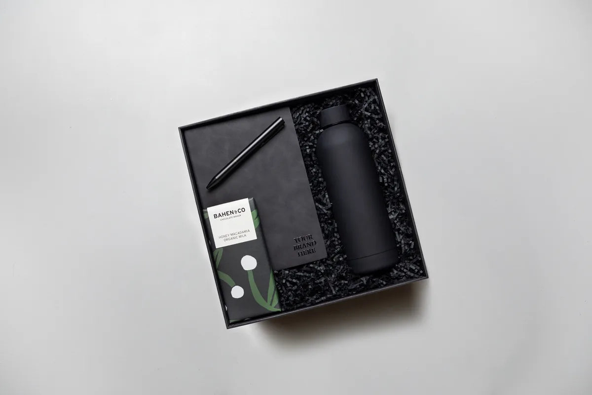 An employee onboarding gift box holding a branded notebook, pen, matte black drink bottle and chocolate, with space to add a company logo.
