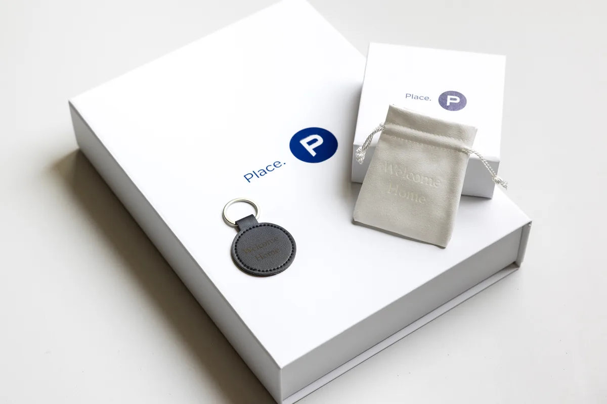 A settlement gift for Place. — a white branded gift box with a Welcome Home leather keyring and a matching suede pouch.