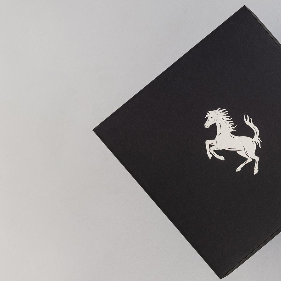 A black rigid gift box with the Ferrari prancing horse hot-foil stamped in white, produced by LÂPACH.